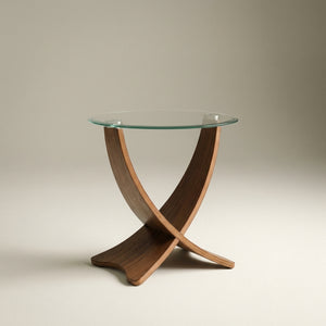 walnut cross legged curved wood lamp table with a clear glass round top in a natural studio setting