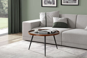Jual Furnishings Siena coffee table displayed individually in a contemporary living room. The table features a round black marble top with white veining, a walnut-finished wooden rim, and slender black metal legs. It is styled in front of a light grey corner sofa with green and white accent cushions, set against a sage green wall with framed black and white prints. A plush grey rug and green curtains complete the elegant decor.