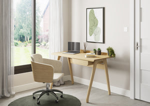 Jual Furnishings home office setup featuring a San Francisco large oak desk and a San Francisco oak fabric office chair. The workspace includes a laptop, books, and potted plants, positioned by a large window with sheer curtains overlooking a green garden.