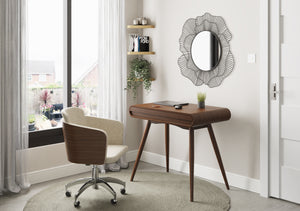 Jual Furnishings PC810 small desk in dark walnut finish, featuring curved edges and tapered legs. The modern home office setup includes a beige swivel chair, a round wireframe mirror, floating shelves, and decorative plants. A large window with sheer curtains allows natural light to brighten the space.