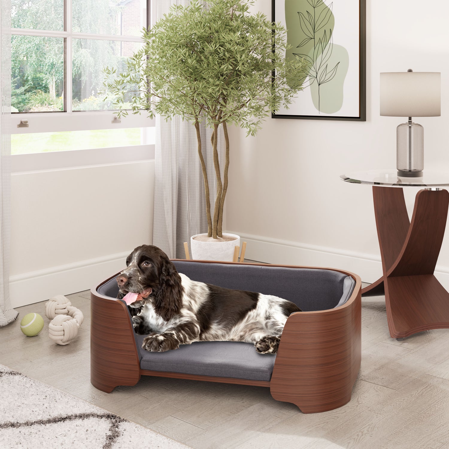 Elegant Jual Furnishings pet bed in walnut wood finish with plush gray cushioning, featuring a relaxed spaniel dog lounging in a stylish modern living space, complemented by a matching curved walnut lamp table for a cohesive design