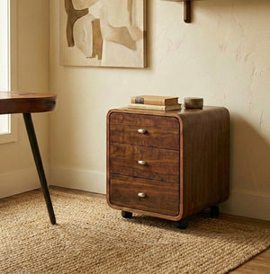 Walnut wooden pedestal with three drawers in a room with a rug and wall art.