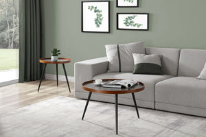 Jual Furnishings Siena walnut and marble room set featuring a round coffee table and a matching side table. Both tables have a smooth walnut-finished wooden rim, black marble top, and slender black metal legs. The set is styled in a modern living room with a light grey corner sofa, green and white accent cushions, and framed botanical prints on a sage green wall. A plush grey area rug and floor-length green curtains complete the elegant, contemporary decor